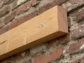 Ein Holzbalken wird mit einer Schraube an einer Ziegelwand befestigt.