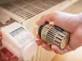 Hände tauschen ein sehr altes Thermostat gegen ein modernes Gerät an einem Heizkörper.