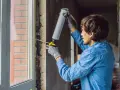 Mann mit Handschuhen und Schaumpistole dichtet den Rahmen für den Fenstertausch ab.