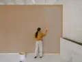 Frau streicht Wand neu. Man fragt sich, wie lange braucht wandfarbe zum trocknen, während sie die helle Farbe aufträgt.
