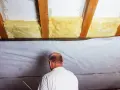 Mann dichtet das Dach von innen ab, indem er Dämmmaterial und eine Folie anbringt.