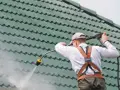 Mann reinigt mit Hochdruckreiniger ein grünes Ziegeldach. Dachreinigung sinnvoll für Langlebigkeit und Optik.