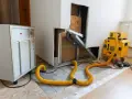 Geräte für technische Trocknung im Einsatz: Ein großer weißer Luftentfeuchter und ein gelbes Gerät mit gelbem Schlauch, die Feuchtigkeit aus einem beschädigten Bereich leiten.