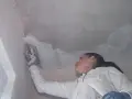 Frau verputzt die Decke mit einer Kelle.
