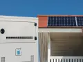 Ein weißer Solarspeicher steht neben einem Haus mit Solarmodulen auf dem Dach. Informieren Sie sich über die Solarspeicher Kosten für Ihre Energieunabhängigkeit.