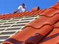 Dachdecker verlegt rote Ziegel. Die Frage "wie lange halten dachziegel" wird durch die Langlebigkeit des Materials beantwortet.