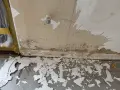 Vorbereitung zum zumauern einer Heizungsnische: abgeplatzter Putz und Schmutz am Boden, Wand mit Wasserflecken und einem Ventil.