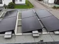 Solarmodule auf einem Bitumen-Flachdach, befestigt mit einer Aufständerung. Ein kleiner schwarzer Kater beobachtet die Installation.