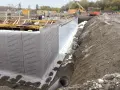 Bauarbeiter bringen Noppenfolie an einer Baugrube an. Die Folie schützt die Wand vor Feuchtigkeit.