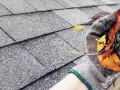 Gefüllte Regenrinne mit Laub und Schmutz, die eine Verstopfung verursacht. Eine Hand in einem Handschuh entfernt das Material.