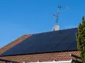 Dach mit Ziegeln, darauf schwarze Solarmodule für HEMS Photovoltaik. Eine Satellitenschüssel und Antenne sind ebenfalls zu sehen.