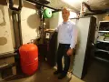 Mann steht neben Heizungsanlage, um Solarthermie zu optimieren. Roter Ausdehnungsbehälter und schwarze Wärmepumpe sichtbar.