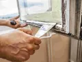 Hände entfernen mit Spachtel alten Fensterkitt. Vorbereitung für das Fensterkitt erneuern.