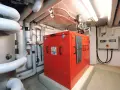 Rotes Blockheizkraftwerk im Keller eines Mehrfamilienhauses, umgeben von Rohren und einer Steuereinheit.