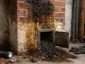 Schwarzer, klebriger Ruß tropft aus einem Kamin. Die Versottung des Kamins ist deutlich sichtbar, mit einer Klappe, die offen steht und noch mehr Ruß freigibt.