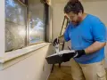 Mann streicht verwittertes Holz am Fenster weiß.