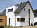 Moderner Neubau trocknet im Sonnenschein. Weiße Fassade, Holzverkleidung und dunkles Dach.