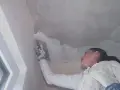 Frau spachtelt mit einem Werkzeug die Betondecke, um sie für die weitere Bearbeitung vorzubereiten.