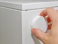 Hand dreht den Regler einer alten Nachtspeicherheizung. Die Bedienung ist einfach, die Zahlen sind gut sichtbar.