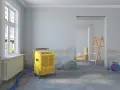 Gelber Bautrockner im Raum, Wände mit Nikotinflecken. Vorbereitung zur **Raucherwohnung renovieren**. Leiter und Kartons im Hintergrund.