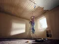 Frau streicht mit einer Teleskopstange und Rolle die Holzpaneele an der Decke weiß.