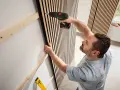 Mann montiert Akustikpaneele an Wand. Tolle Ideen für moderne Raumgestaltung und Schallschutz.