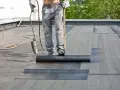 Arbeiter verlegt mit Brenner und Rolle Dachpappe. Die Hitze schmilzt die Unterseite, um eine wasserdichte Abdichtung zu schaffen.