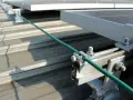 Detailaufnahme der Erdung einer PV-Anlage. Ein grünes Kabel wird sicher mit einer Klemme an der Aluminiumkonstruktion befestigt, die die Solarmodule auf dem Dach hält.
