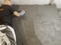 Mann trägt Mörtel auf, um die Kellerwand von innen abzudichten. Die Wand ist bereits teilweise verputzt.
