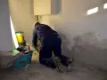 Bauarbeiter kniet vor einer nassen Wand, umgeben von Eimern und Werkzeugen.