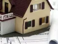 Modell eines Einfamilienhauses auf Bauplänen, daneben zwei aufgerollte Pläne. Ein Baukasten-BHKW könnte hier integriert werden.