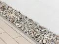 Kiesbett als Spritzschutz am Haus, neben gepflastertem Weg.