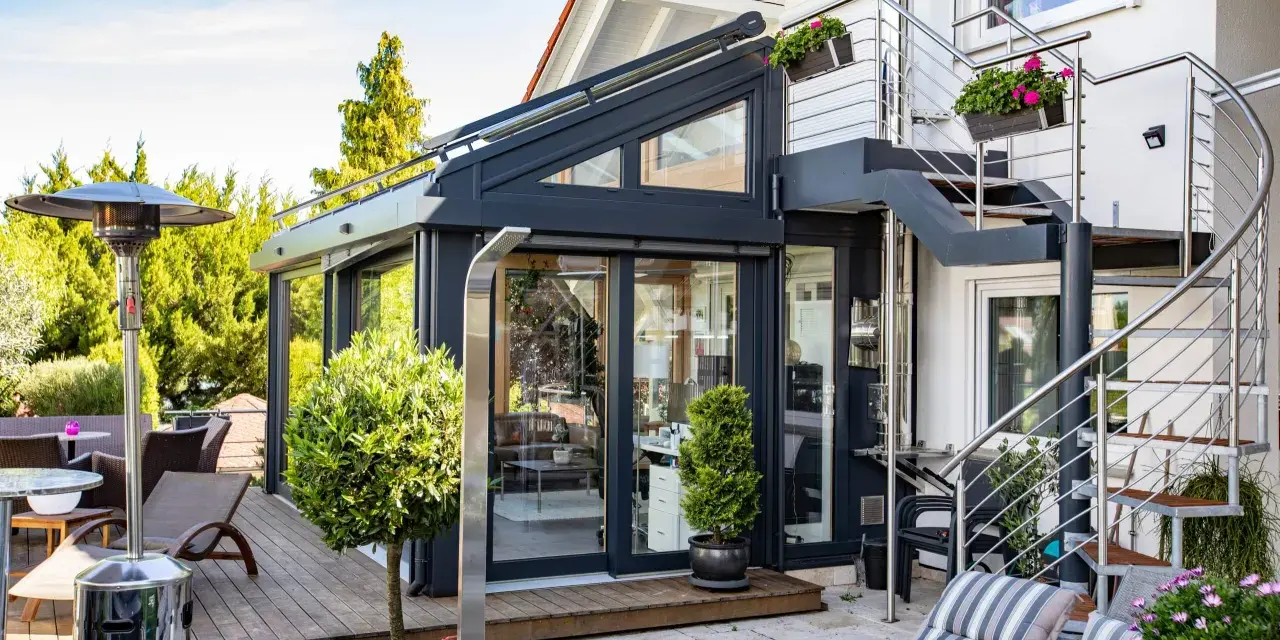 Moderner Wintergarten mit Außentreppe und Terrassenmöbeln. Ein Heizpilz sorgt für Wärme.