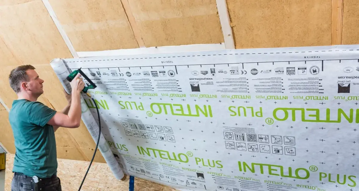 Mann bringt mit einem Tacker eine Dampfbremse an der Dachschräge an. Die Folie ist mit "INTELLO PLUS" bedruckt.