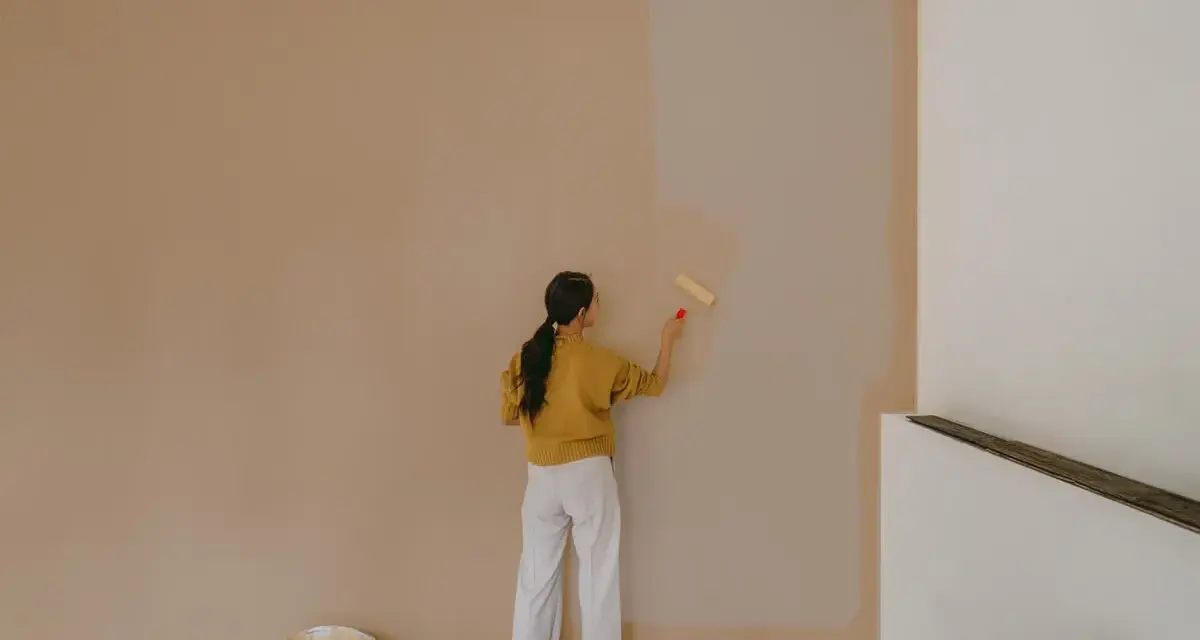 Frau streicht Wand neu. Man fragt sich, wie lange braucht wandfarbe zum trocknen, während sie die helle Farbe aufträgt.