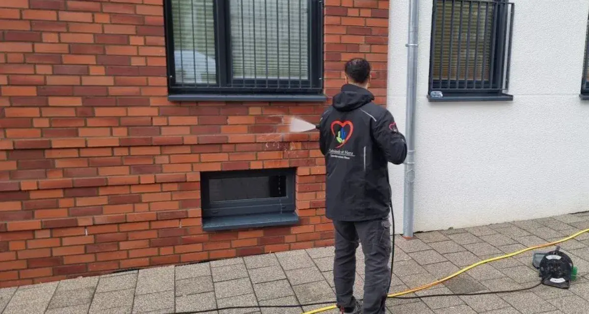 Mann reinigt mit Hochdruckreiniger die Ziegel-Fassade.