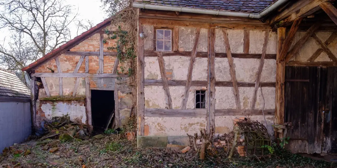 Ein altes Fachwerkhaus wartet auf seine Sanierung. Die Holzbalken und Lehmwände zeigen deutliche Spuren der Zeit.