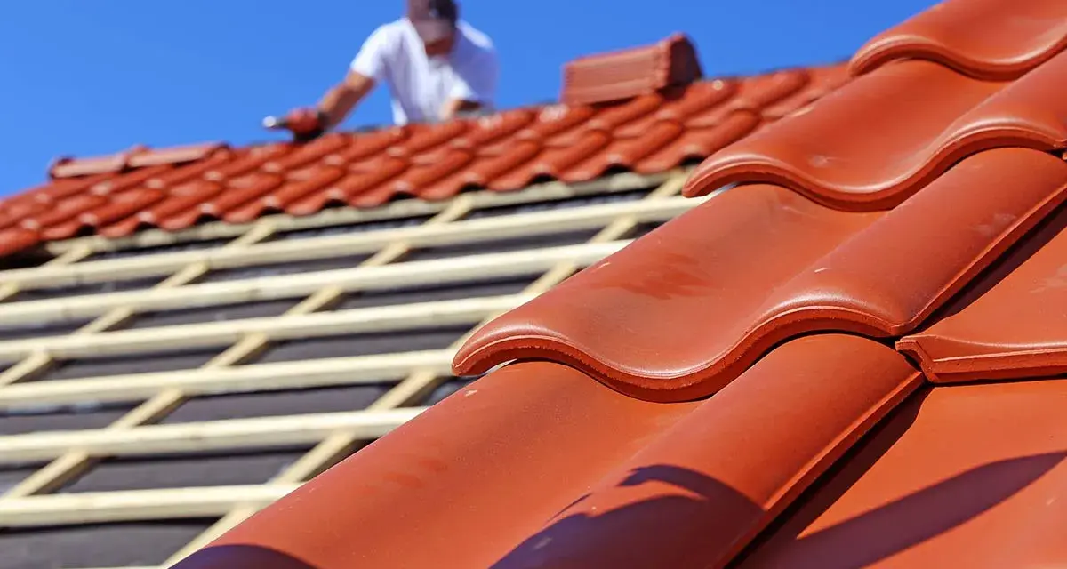 Dachdecker verlegt rote Ziegel. Die Frage "wie lange halten dachziegel" wird durch die Langlebigkeit des Materials beantwortet.