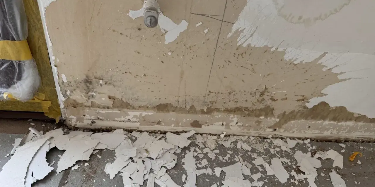 Vorbereitung zum zumauern einer Heizungsnische: abgeplatzter Putz und Schmutz am Boden, Wand mit Wasserflecken und einem Ventil.