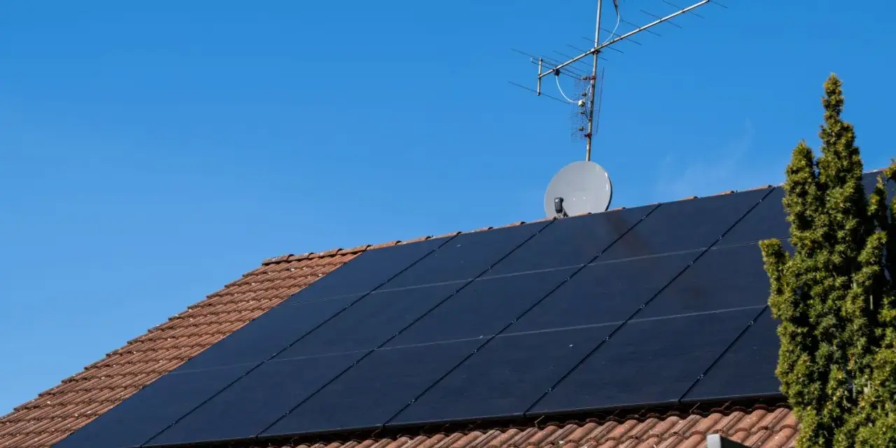 Dach mit Ziegeln, darauf schwarze Solarmodule für HEMS Photovoltaik. Eine Satellitenschüssel und Antenne sind ebenfalls zu sehen.
