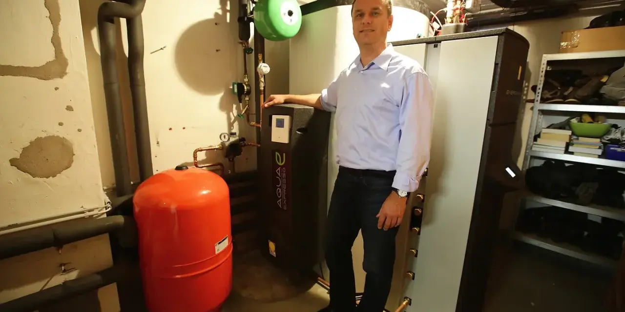 Mann steht neben Heizungsanlage, um Solarthermie zu optimieren. Roter Ausdehnungsbehälter und schwarze Wärmepumpe sichtbar.