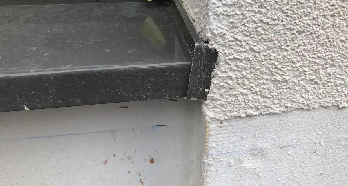 Detailaufnahme einer Fensterbank, die mit Klebeband provisorisch abgedichtet ist. Die raue Fassade und die graue Fensterbank sind gut erkennbar.