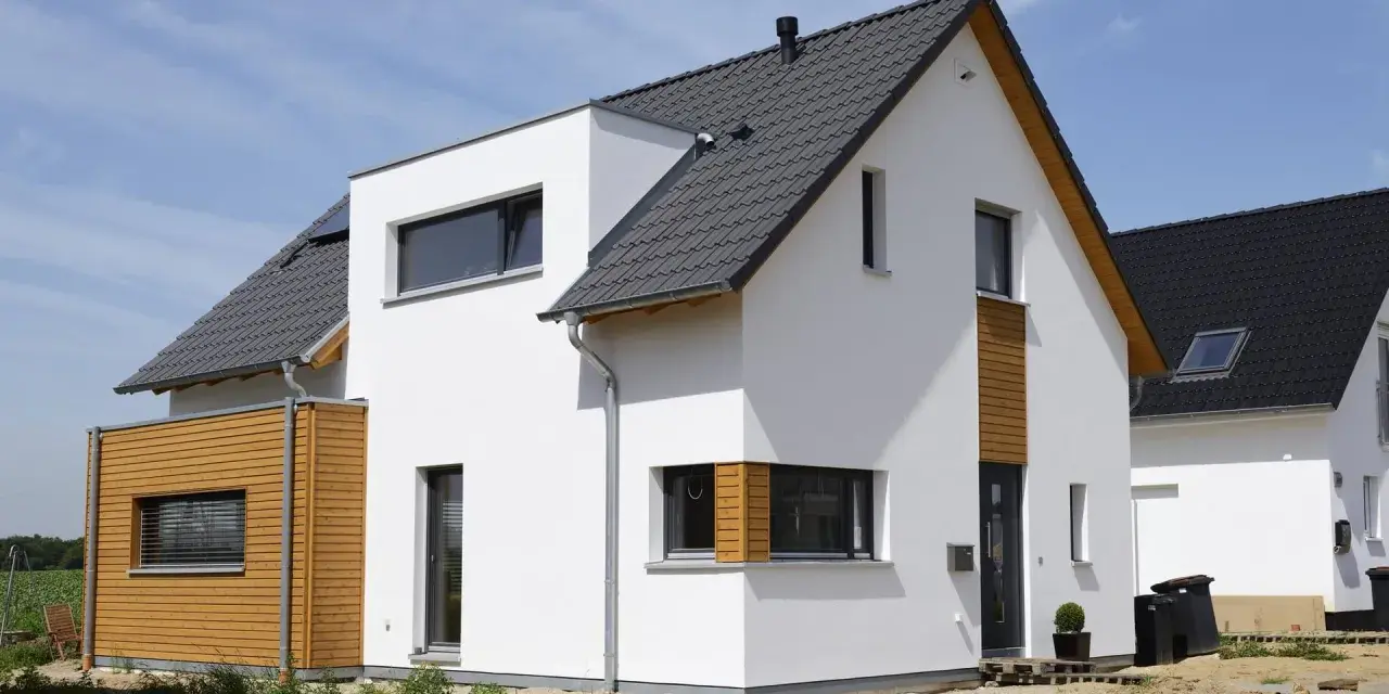 Moderner Neubau trocknet im Sonnenschein. Weiße Fassade, Holzverkleidung und dunkles Dach.