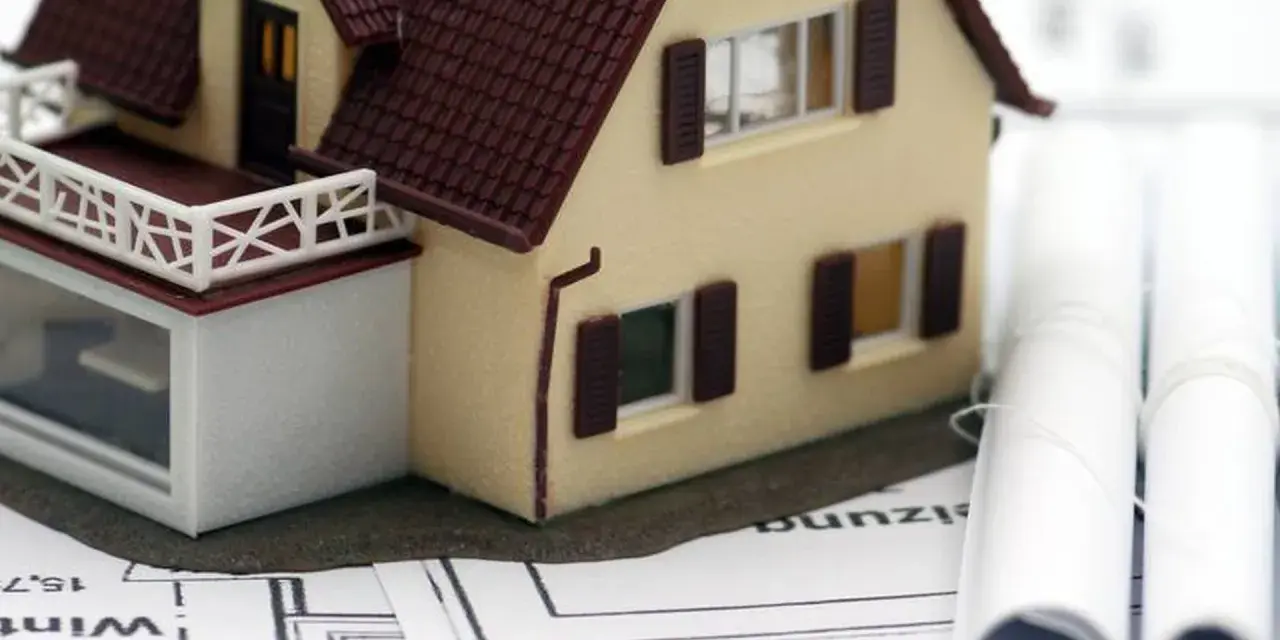 Modell eines Einfamilienhauses auf Bauplänen, daneben zwei aufgerollte Pläne. Ein Baukasten-BHKW könnte hier integriert werden.
