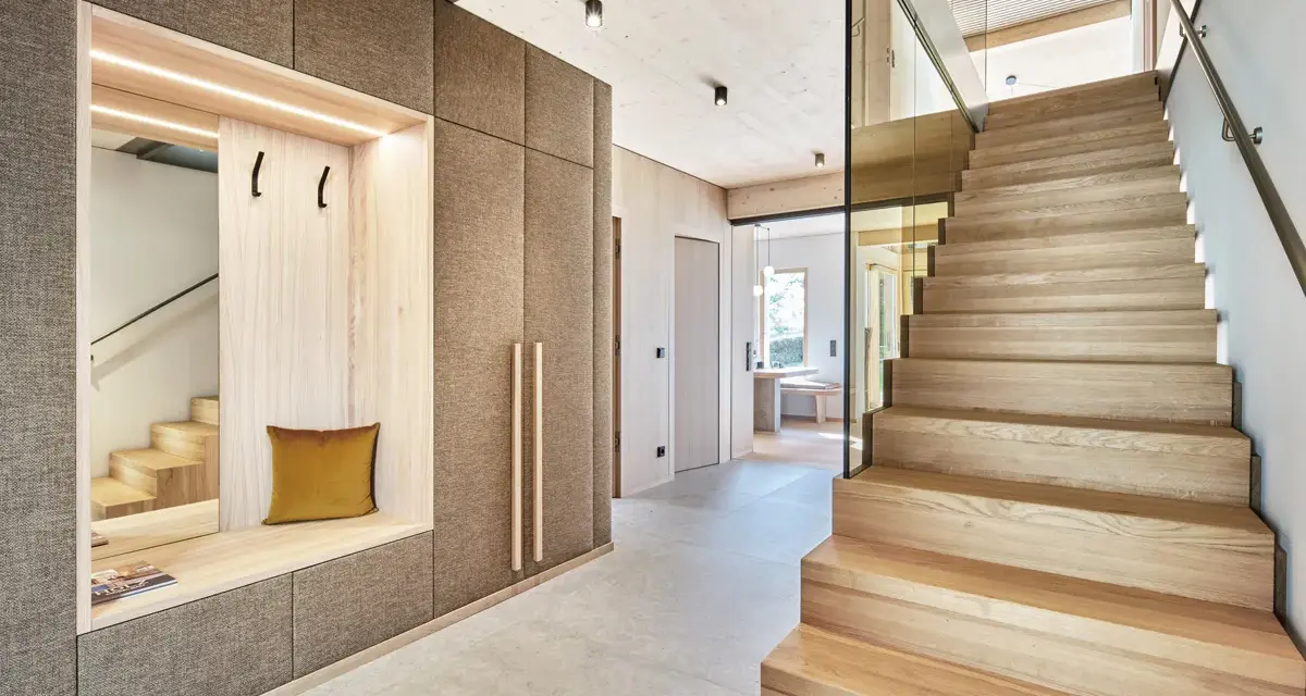 Moderne Diele mit Sitzbank und Garderobe, die Treppe aus verschiedenen **Hartholzarten** strahlt Wärme aus.