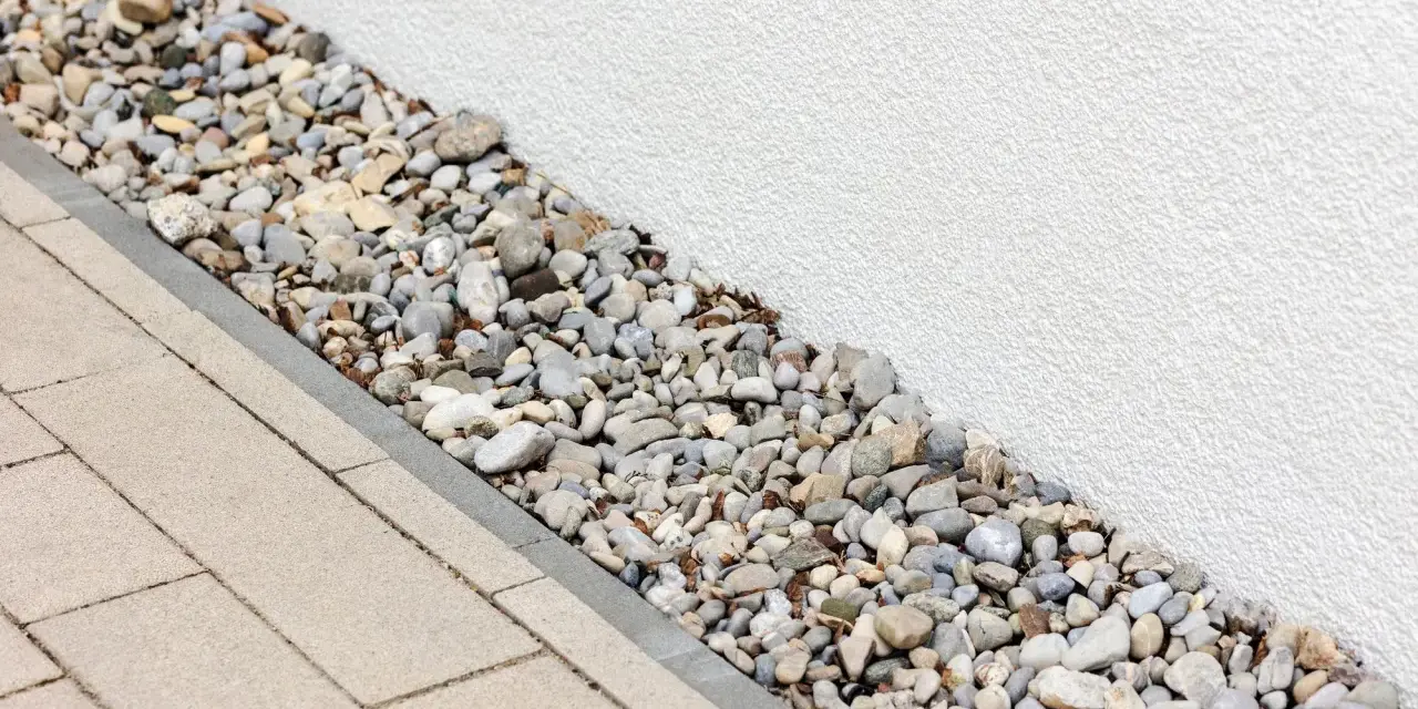 Kiesbett als Spritzschutz am Haus, neben gepflastertem Weg.