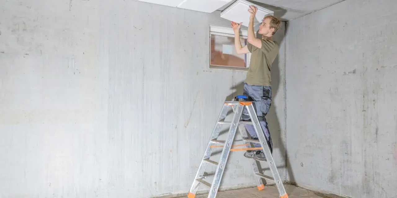 Mann auf Leiter montiert weiße Platten zur kellerdecke isolieren.