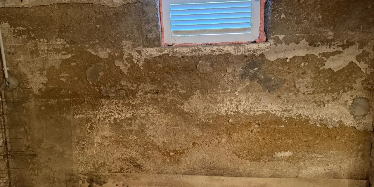 Feuchte Wände im Keller eines alten Hauses, deutet auf Grundwasser im Keller hin. Ein kleines Fenster ist sichtbar.