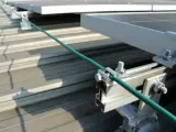Detailaufnahme der Erdung einer PV-Anlage. Ein grünes Kabel wird sicher mit einer Klemme an der Aluminiumkonstruktion befestigt, die die Solarmodule auf dem Dach hält.