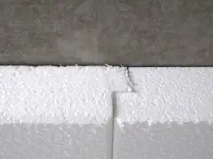 Detailaufnahme: Styrodur kleben an einer Betonwand. Die weißen Styroporplatten sind präzise zugeschnitten und stoßen nahtlos aneinander.